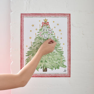 Photo of a child placing a letter sticker on the Advent Alphabet Calendar by The Letter Nest, hanging on a white brick wall