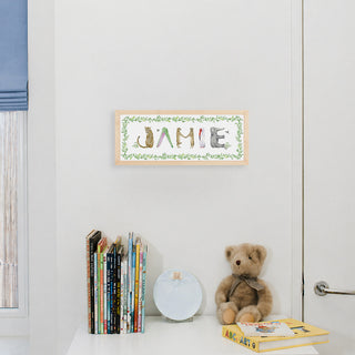 Custom Animal Name Print by The Letter Nest spelling "Jamie" in animal letters shown in a nursery in a natural frame with vine border