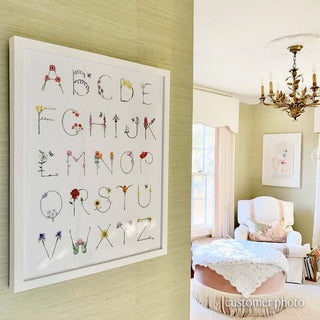 Flower Alphabet by The Letter Nest in a white frame hanging in an elegant nursery with sage green grasscloth wallpaper, featuring blooms from A to Z. 