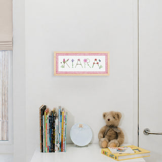 Custom Flower Name Print by The Letter Nest in flower letters spelling "Kiara" with a pink gingham border in a natural frame hung up in a nursery