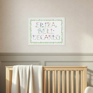 Nursery room with wooden crib, rocking chair, and framed Full Name Print by The Letter Nest in flower letters, vine border, and a white frame