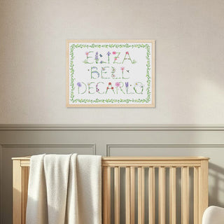 Nursery room with wooden crib, rocking chair, and framed Full Name Print by The Letter Nest in a natural frame with flower letters and a vin border