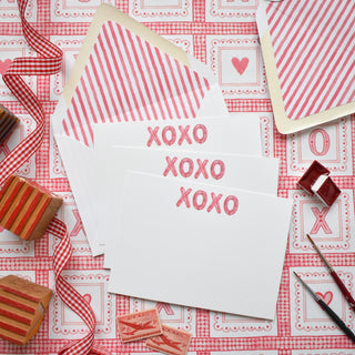 Flatlay styled photo of The Letter Nest's hand-painted, printed watercolor cards featuring stylized "XOXO" Balloon Letters at the top, with pink stripe envelopes