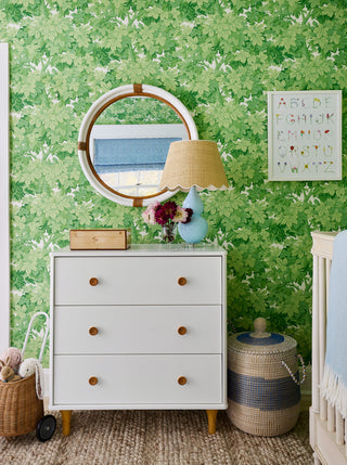 Nursery with green leaf wallpaper, a white dresser, round mirror and an alphabet print by The Letter Nest
