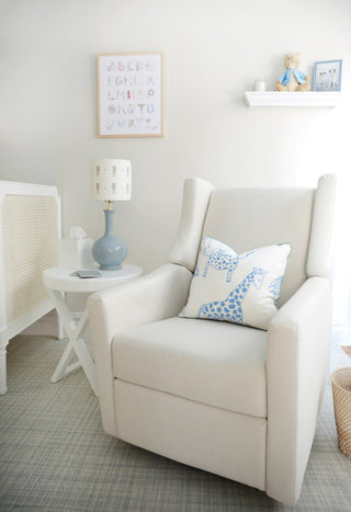 White nursery glider with a giraffe pillow beneath a framed alphabet print by The Letter Nest