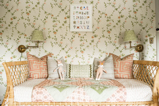 Rattan daybed with pink and green pillows below a hand-painted alphabet print by The Letter Nest on floral wallpaper