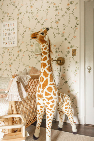 Giraffe plush and rattan chair in a nursery with floral wallpaper and a hand-painted alphabet print by The Letter Nest